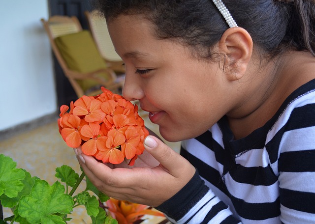 Niña oliendo una flor de geranio